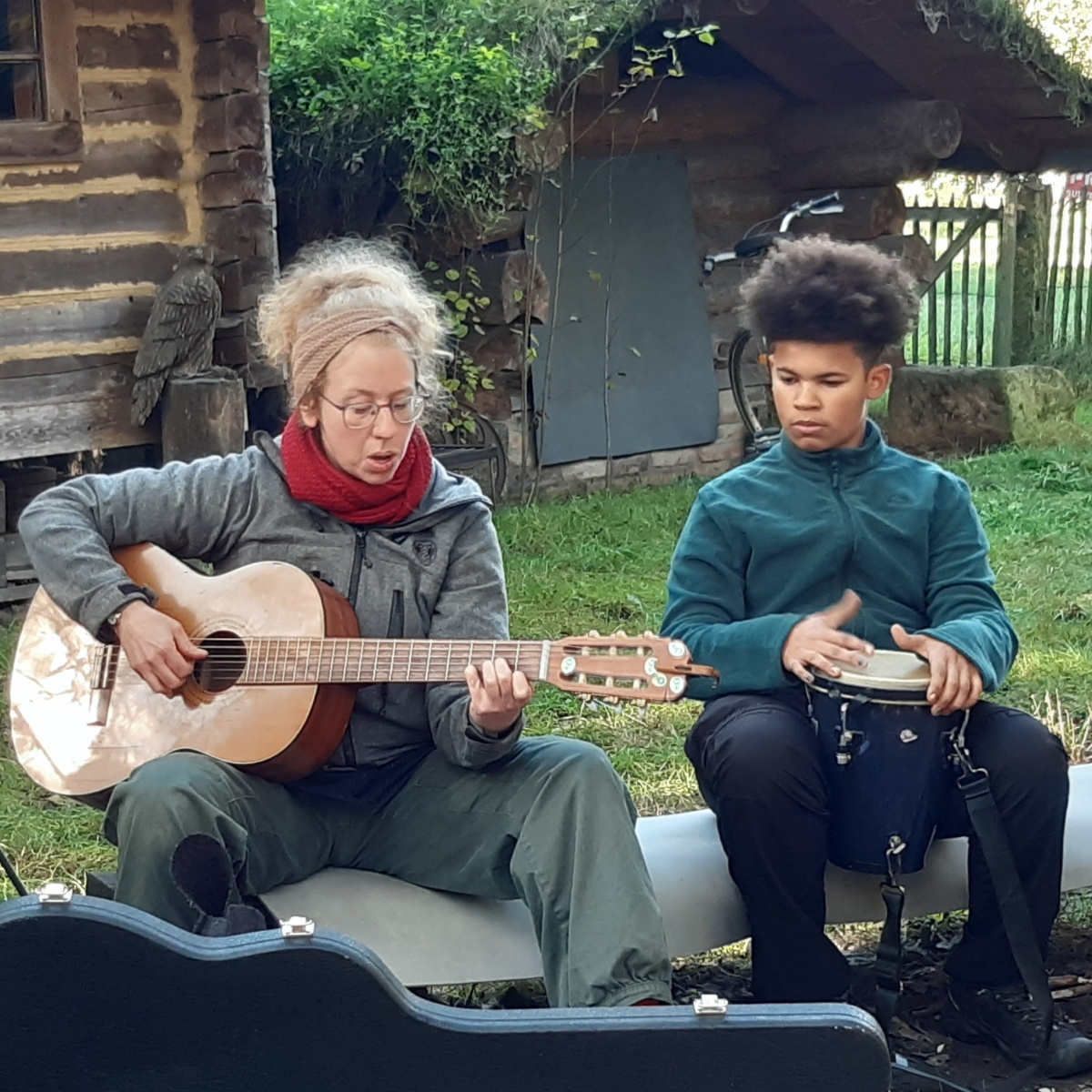 Menschen musizieren im Freien mit Gitarre und Trommel.