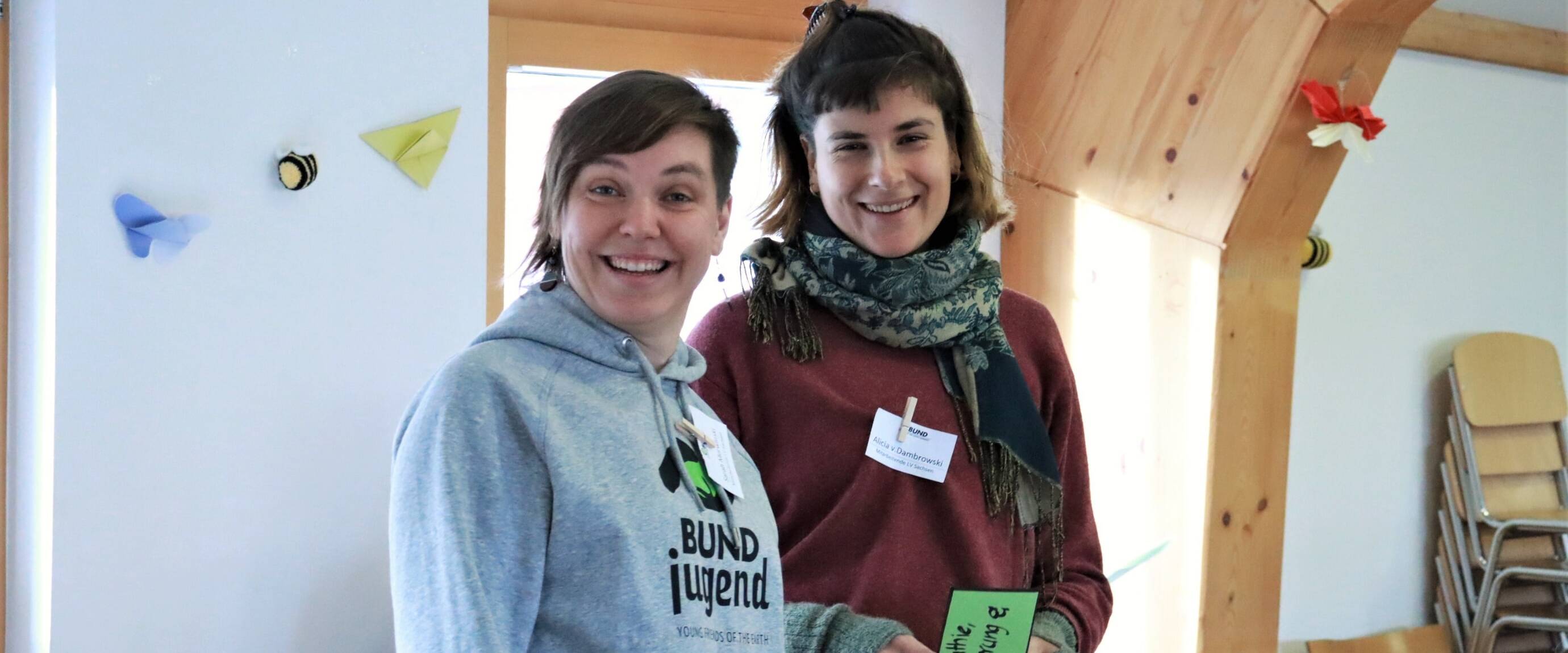 Zwei Personen lächelnd bei Indoor-Veranstaltung.