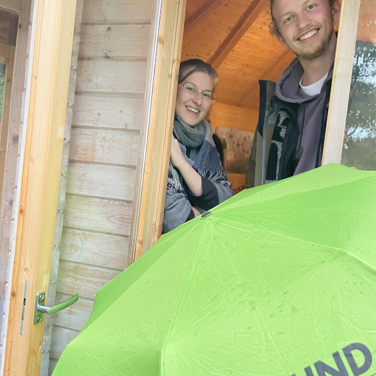 Zwei Menschen im Türrahmen mit grünem Regenschirm