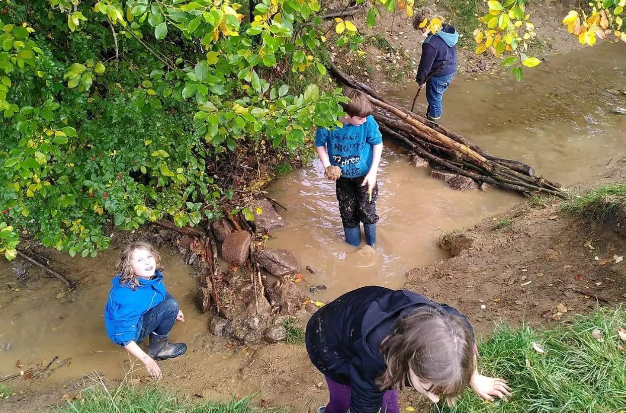 Kinder spielen im Bach mit Matsch und Wasser.